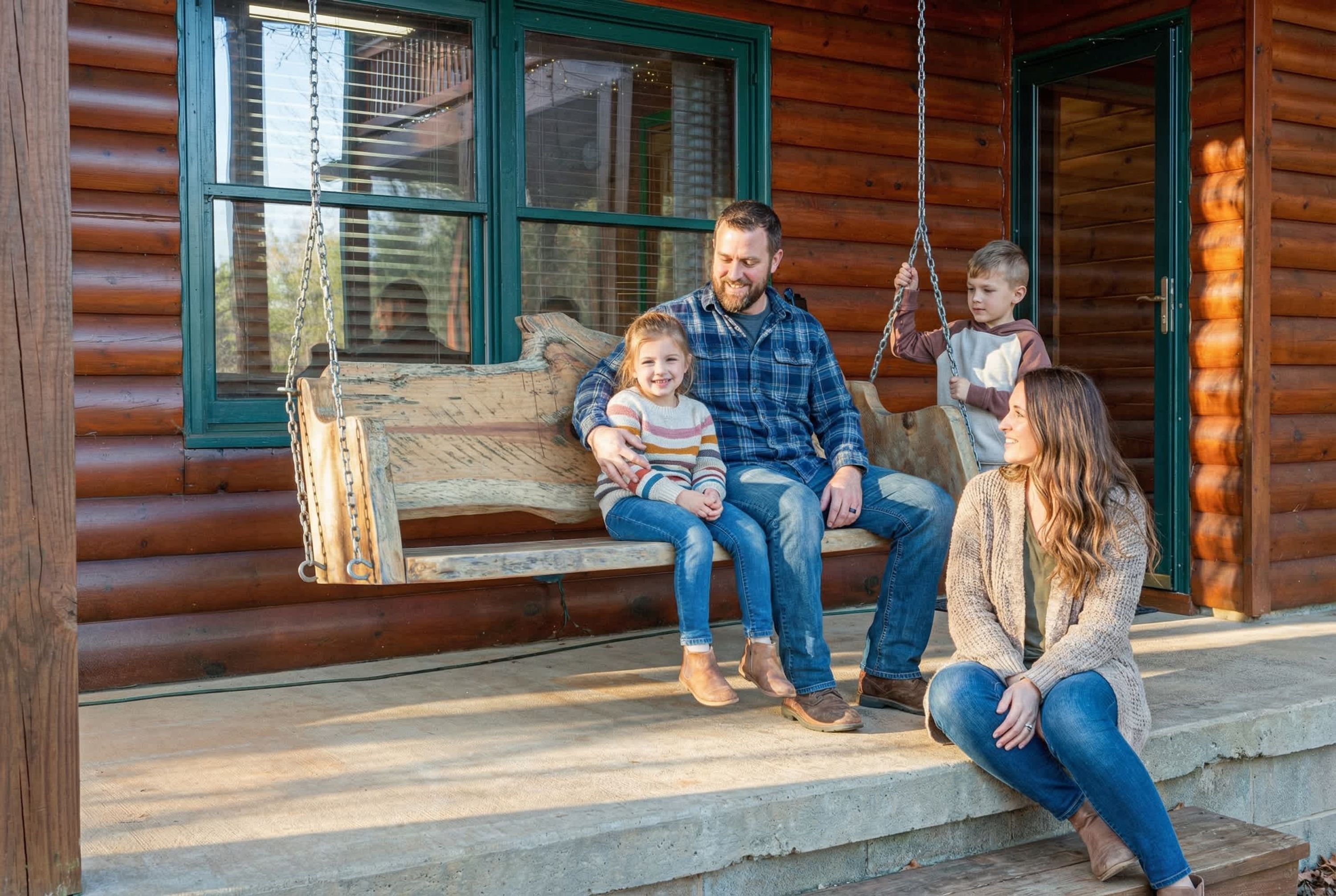 A family on a wooden porch with a swing, a log cabin exterior, and a window with blinds.
