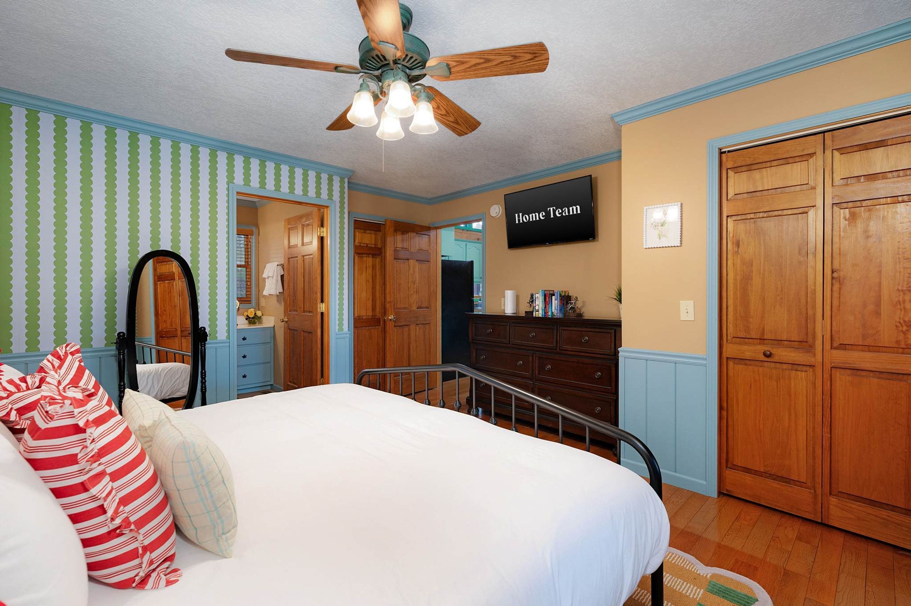 A bedroom with a bed, a ceiling fan, a dresser, and a television on the wall.
