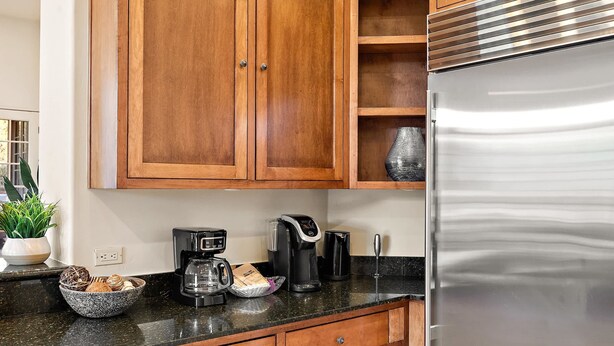 Eine Küche mit Holzschränken, einem Edelstahl-Kühlschrank, einer Kaffeemaschine und einer schwarzen Arbeitsplatte.