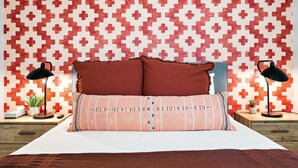 Ein Schlafzimmer mit einer gemusterten Wand, einem Bett mit zwei Kissen, zwei Nachttischlampen und einem Nachttisch mit einer Pflanze.