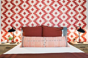 Ein Schlafzimmer mit einer gemusterten Wand, einem Bett mit zwei Kissen, zwei Nachttischlampen und einem Nachttisch mit einer Pflanze.