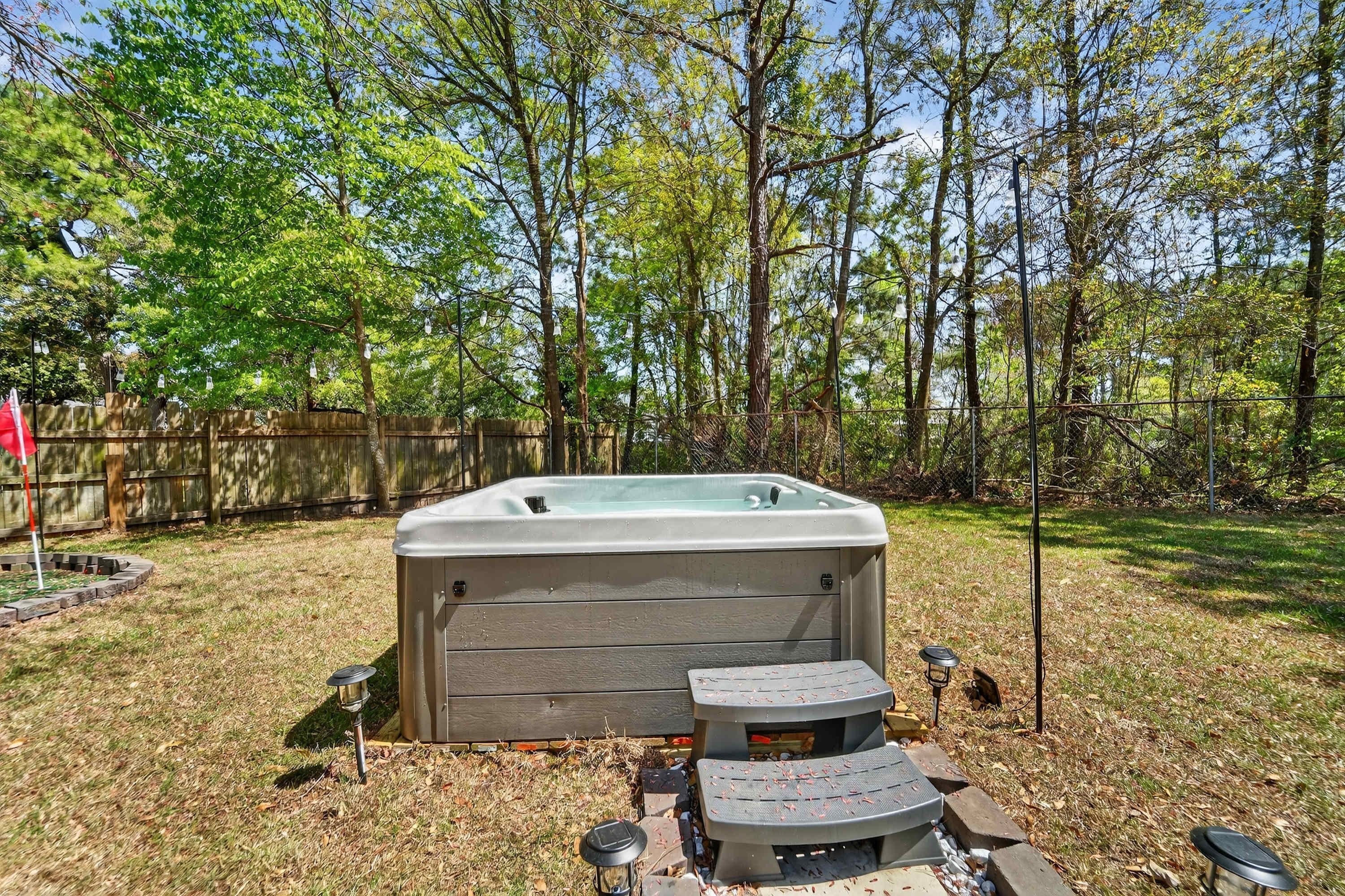 A hot tub in a backyard with a wooden deck and a fence.