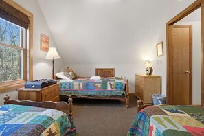 Un dormitorio con dos camas, una ventana con persianas, una lámpara, un tocador de madera y una puerta.