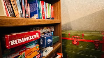 A bookshelf with books and games, including a red box labeled 'RUMMKB' and a green trunk with red straps.