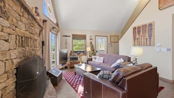 A cozy living room with a stone wall, a fireplace, a television, a sofa, and a coffee table.