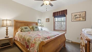 A bedroom with a wooden bed, a ceiling fan, a window with a view, and a painting on the wall.