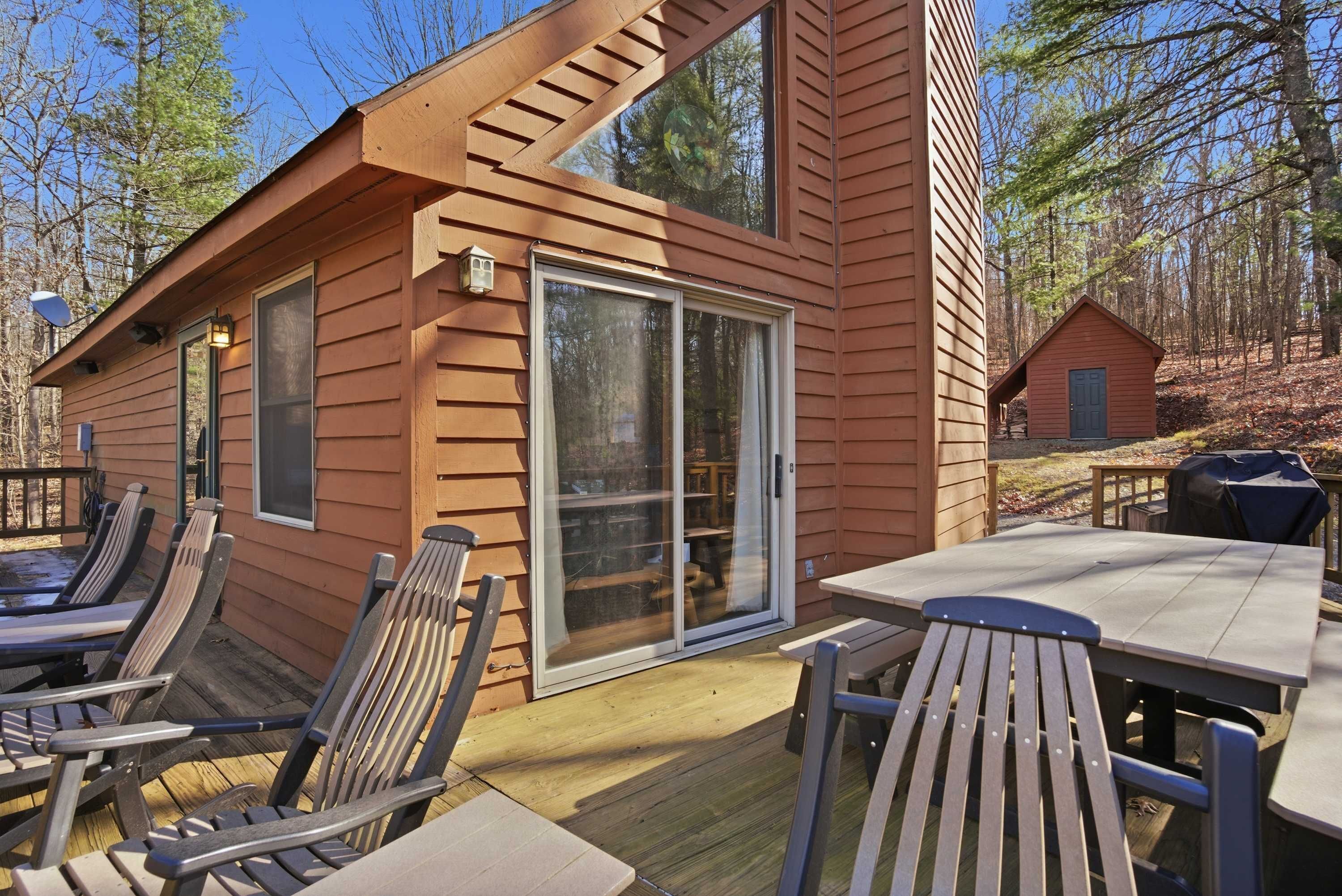 A wooden cabin with a deck, outdoor seating, and a sliding glass door.