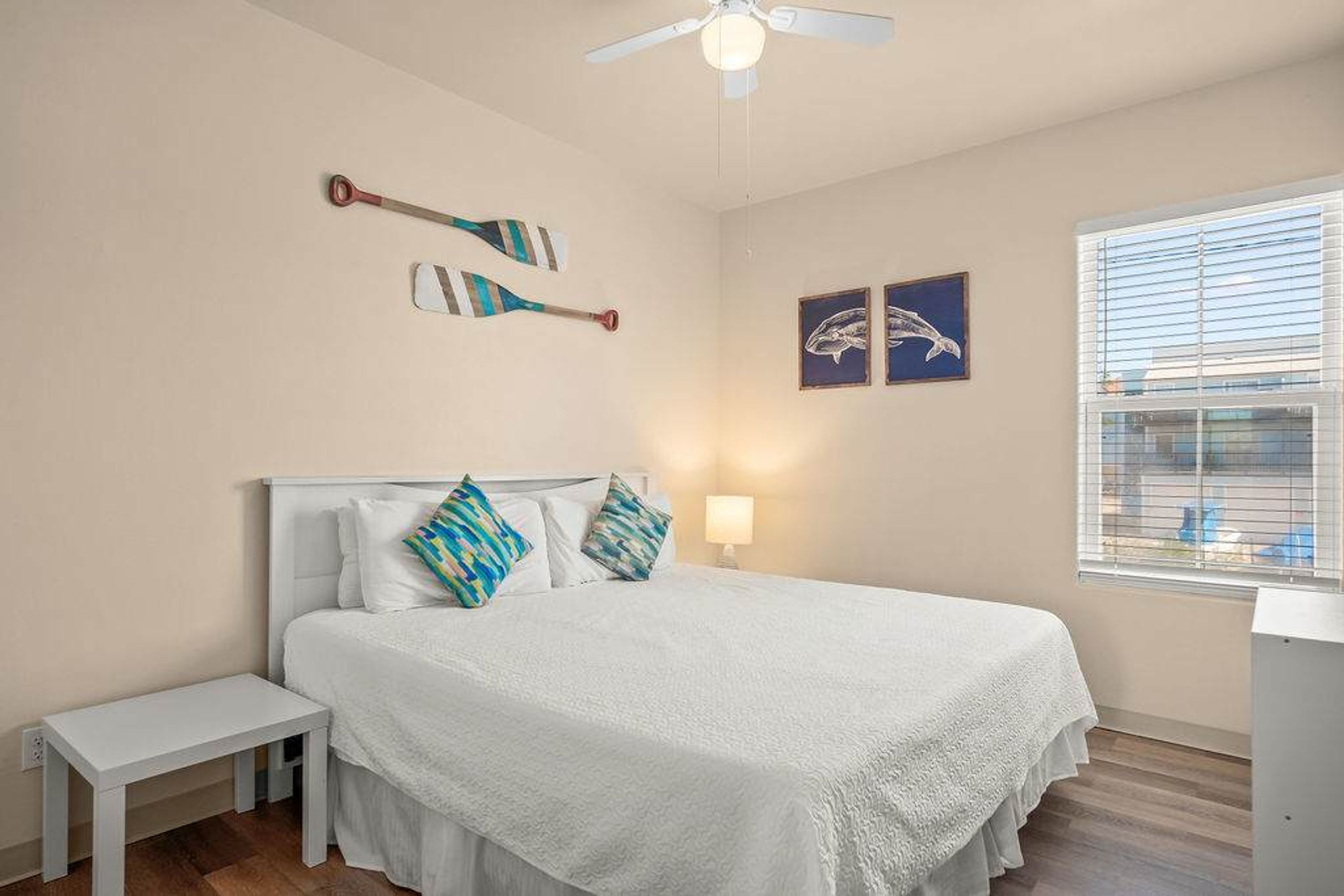 Une chambre à coucher avec un lit, une table de chevet, un ventilateur de plafond et des œuvres d’art accrochées aux murs.