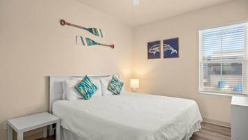 A bedroom with a bed, a bedside table, a ceiling fan, and artwork on the walls.