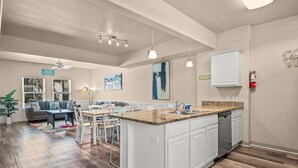 Een ruime keuken met een centraal eiland, witte kasten en een eethoek met een tafel en stoelen.