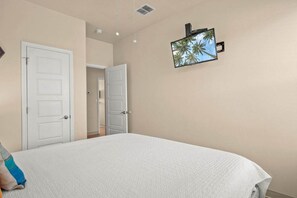Un dormitorio con una cama, televisión montada en la pared y dos puertas.