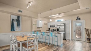Een moderne keuken met een eethoek, bestaande uit een houten tafel en stoelen, een bar met krukken, en een koelkast.