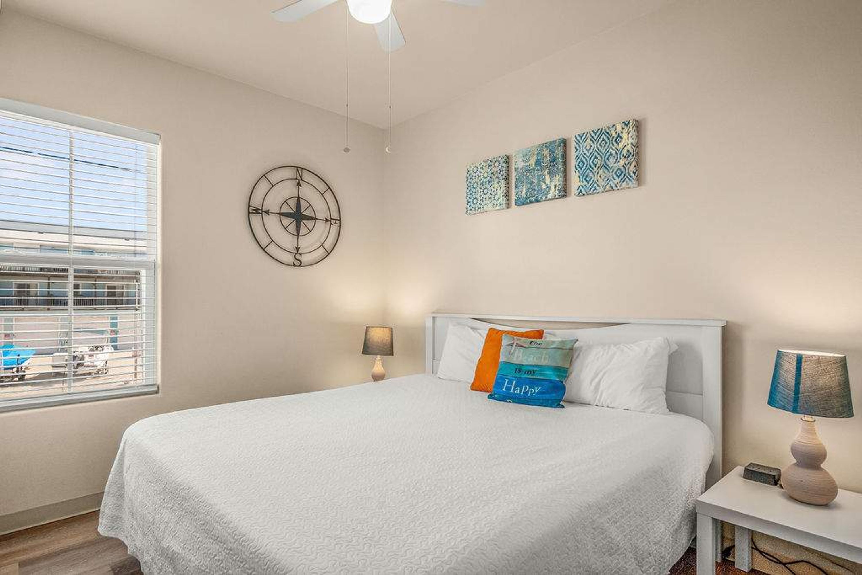 Una camera da letto con un letto, due comodini, una finestra con persiane, una ventola a soffitto e decorazioni alle pareti.