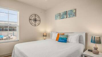 Een slaapkamer met een bed, twee nachtkastjes, een raam met zonwering, een plafondventilator en wanddecoratie.