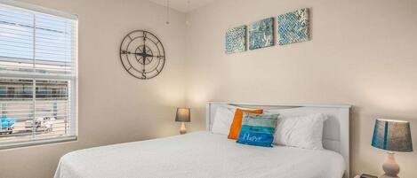 Un dormitorio con una cama, dos mesitas de noche, una ventana con persianas, un ventilador de techo y decoración en la pared.