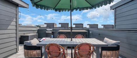 A rooftop patio with a table, chairs, and an umbrella.