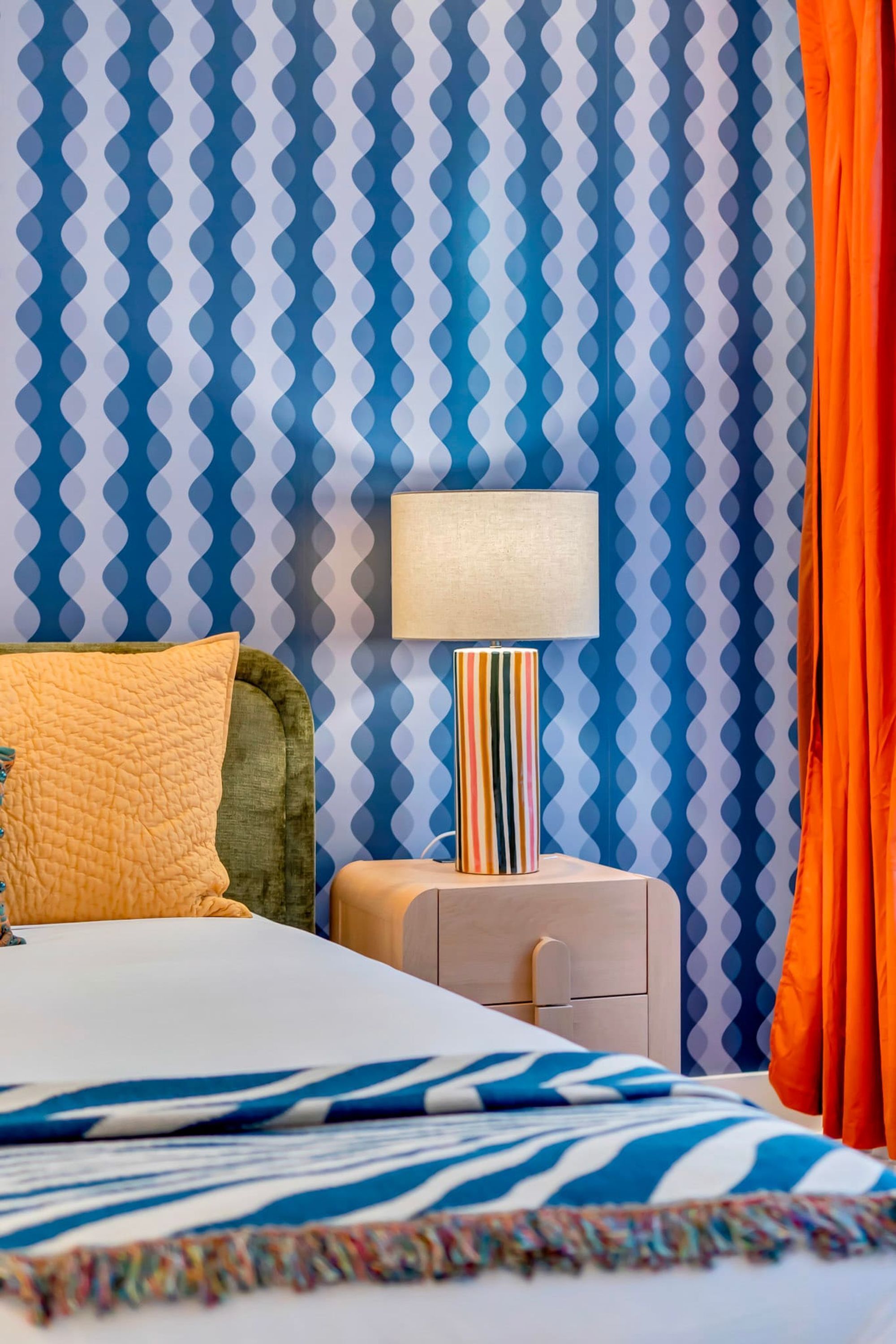 A hotel room with a bed, a bedside lamp, and a patterned wall.