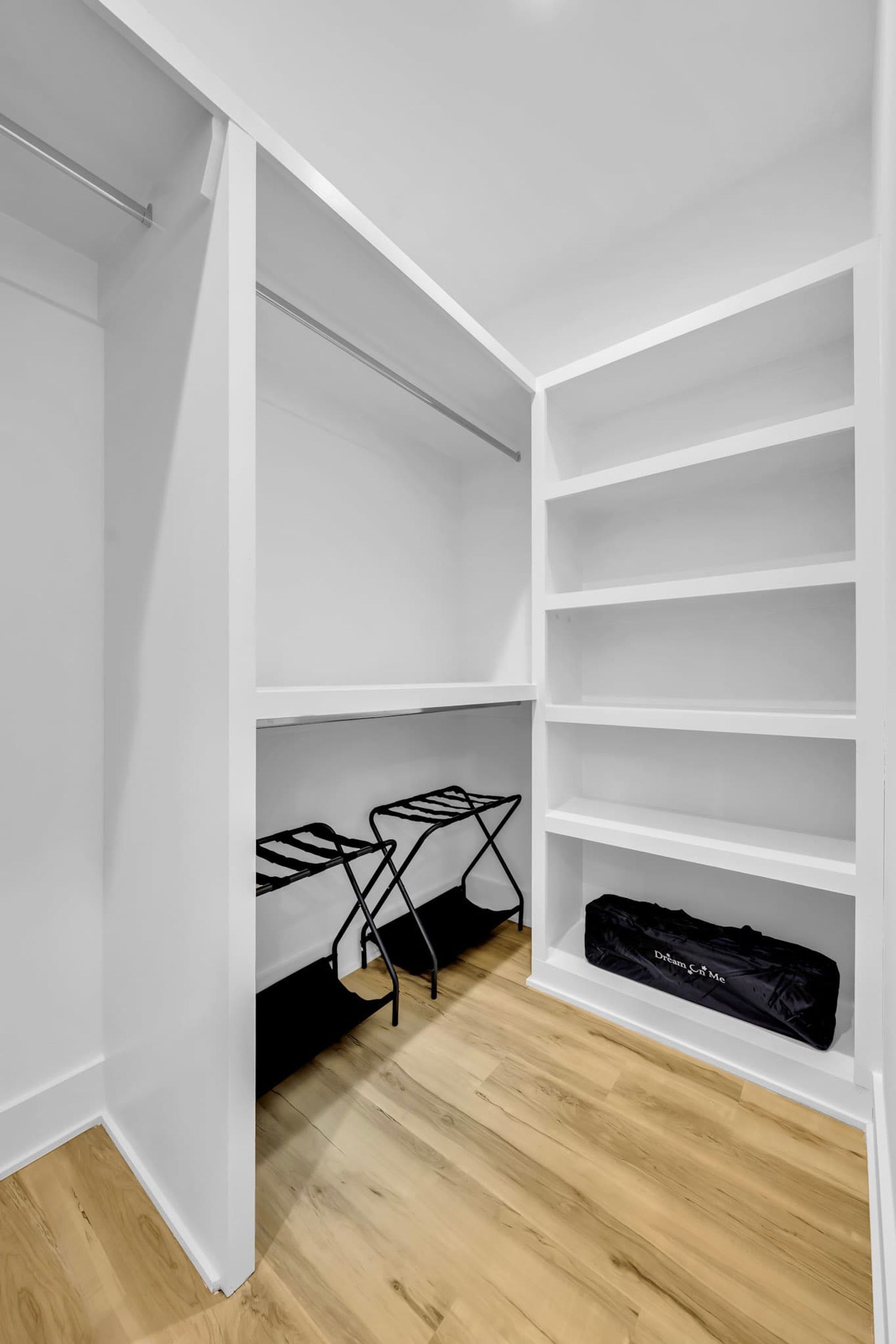 A walk-in closet with white shelving and a black drying rack on the floor.