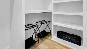 Un vestidor con estanterías blancas y un tendedero negro en el suelo.