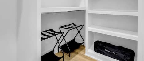 Un vestidor con estanterías blancas y un tendedero negro en el suelo.