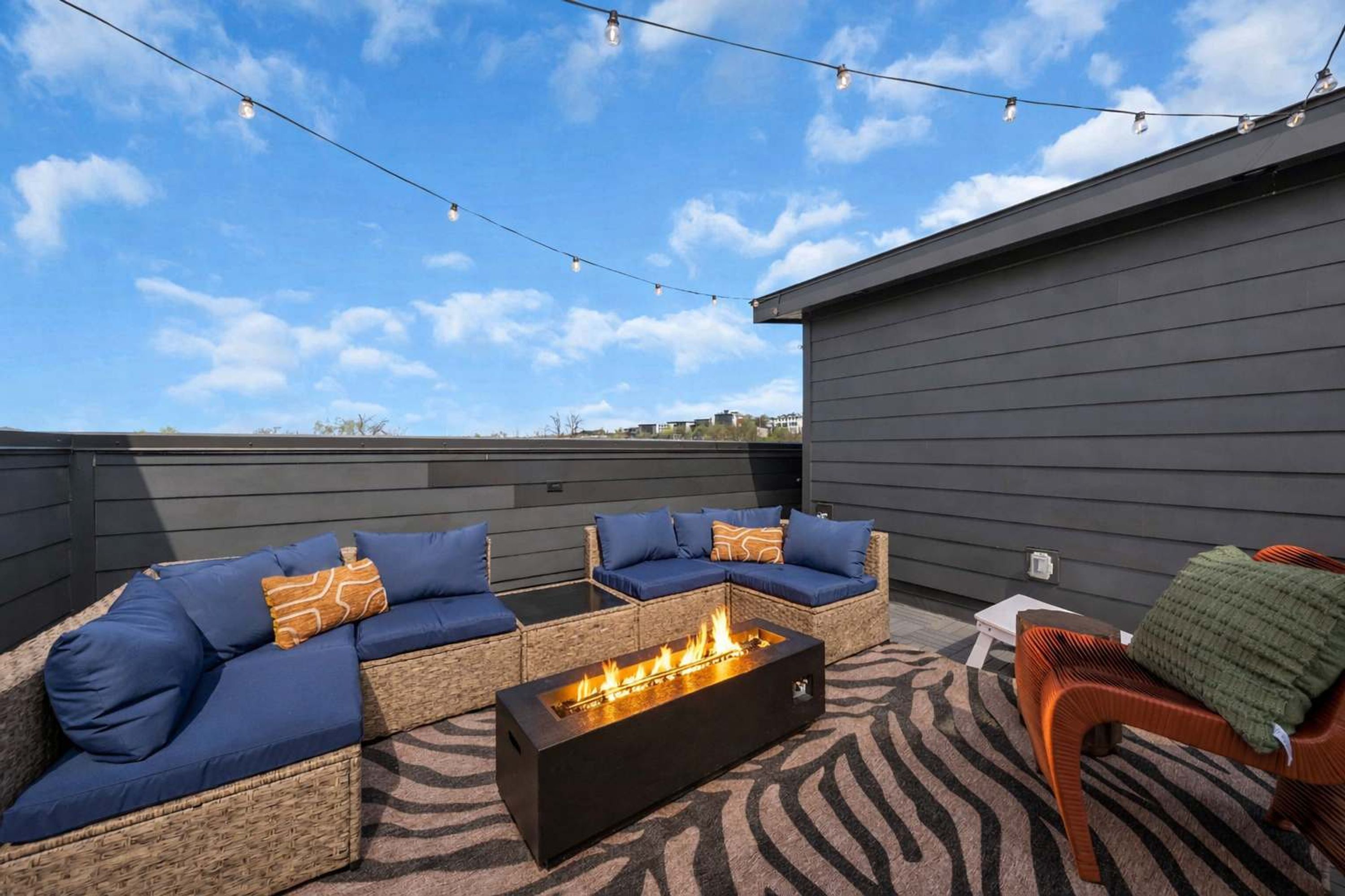 An outdoor seating area with a fire pit, string lights, and a view of the sky.
