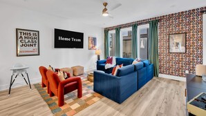 Ein modernes Wohnzimmer mit einem blauen Sofa, roten Sessel und einem weißen Hochstuhl, an der Wand ein Muster.