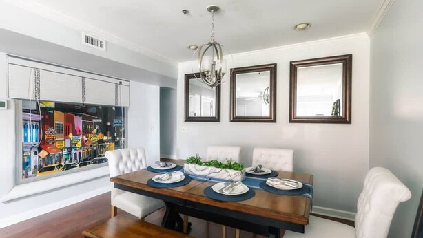Un comedor con una mesa de madera dispuesta para cuatro, sillas blancas tapizadas y dos espejos colgados en la pared.