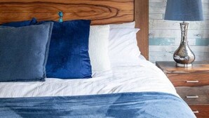 Una cama con cabecera de madera, almohadas azules y una colcha blanca.