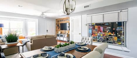 A dining area with a wooden table set for four, a ceiling fan, and a view of a street through a window with blinds.