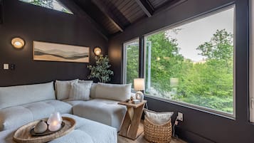 A modern living room with a large window, a sofa, a lamp, and a painting on the wall.