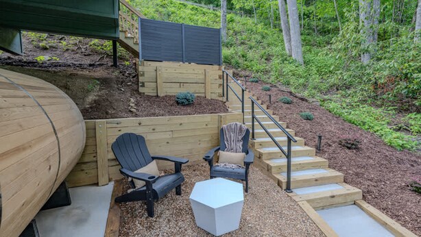 Eine Holzterrasse mit Sitzgelegenheiten im Freien, einer Treppe und Blick auf eine bewaldete Landschaft.