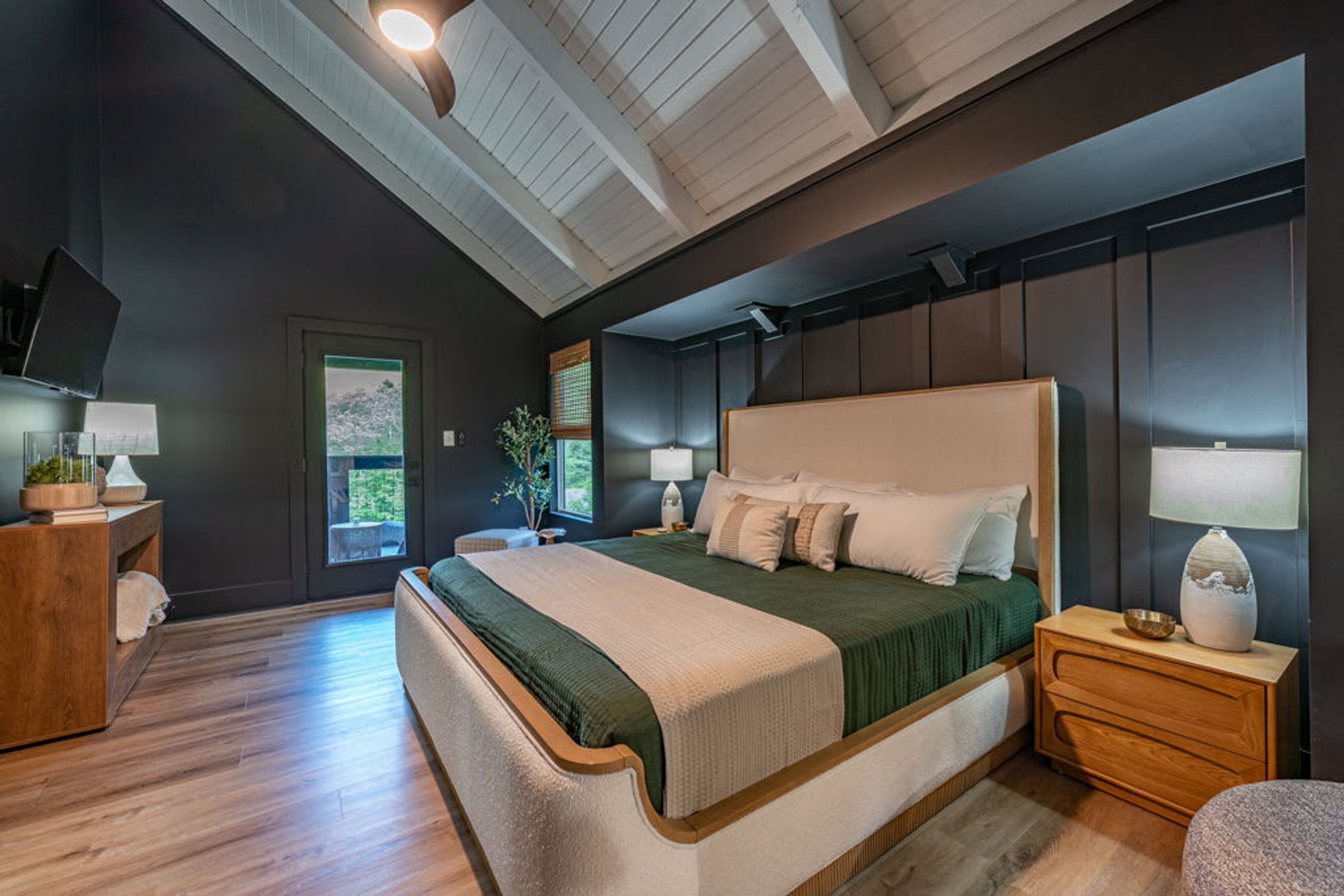 A modern bedroom with a large bed, bedside tables, a TV, and a window with a view.