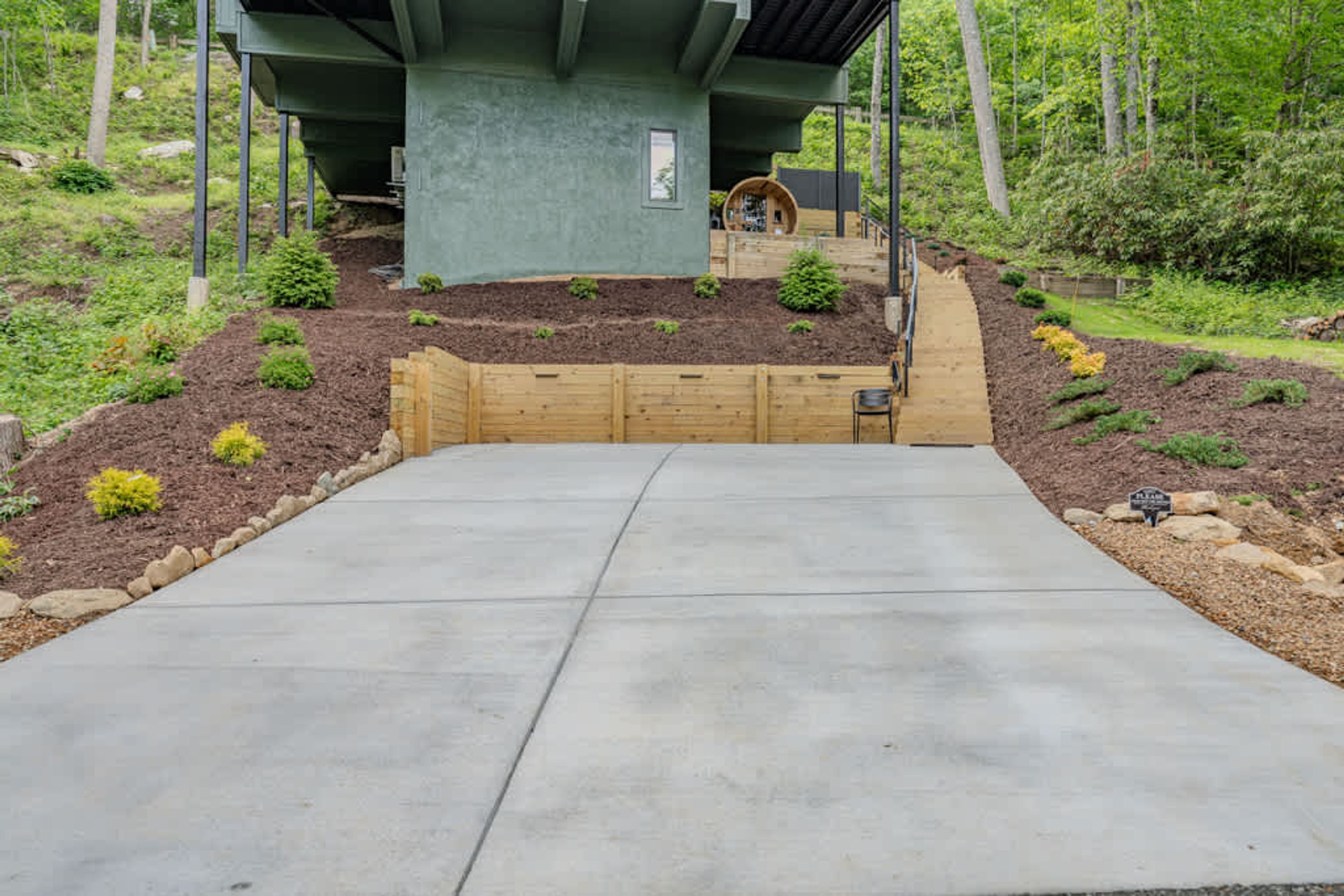 A concrete driveway leading to a wooden deck with a raised garden area.