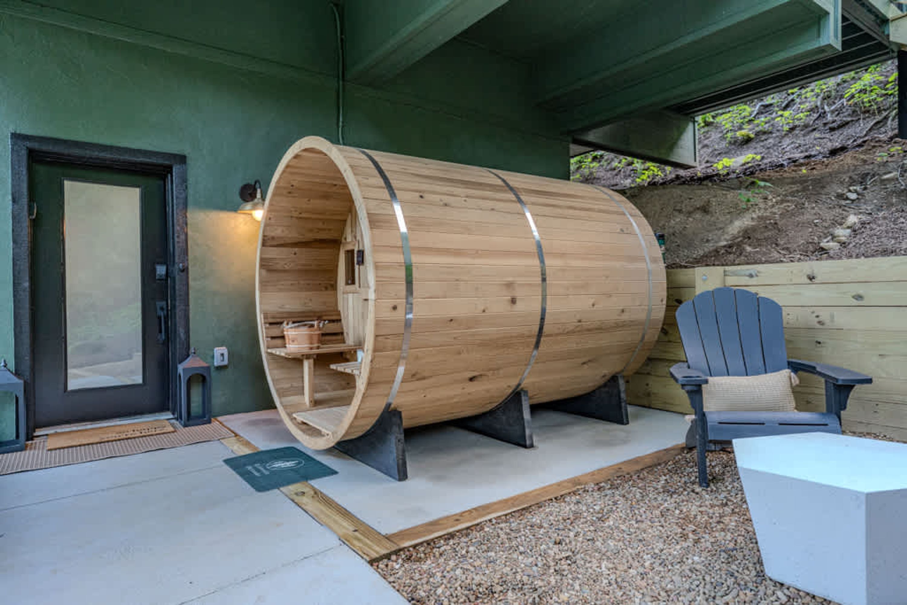 Una sauna de diseño en forma de barril de madera, con puerta, una silla y una pequeña mesa.