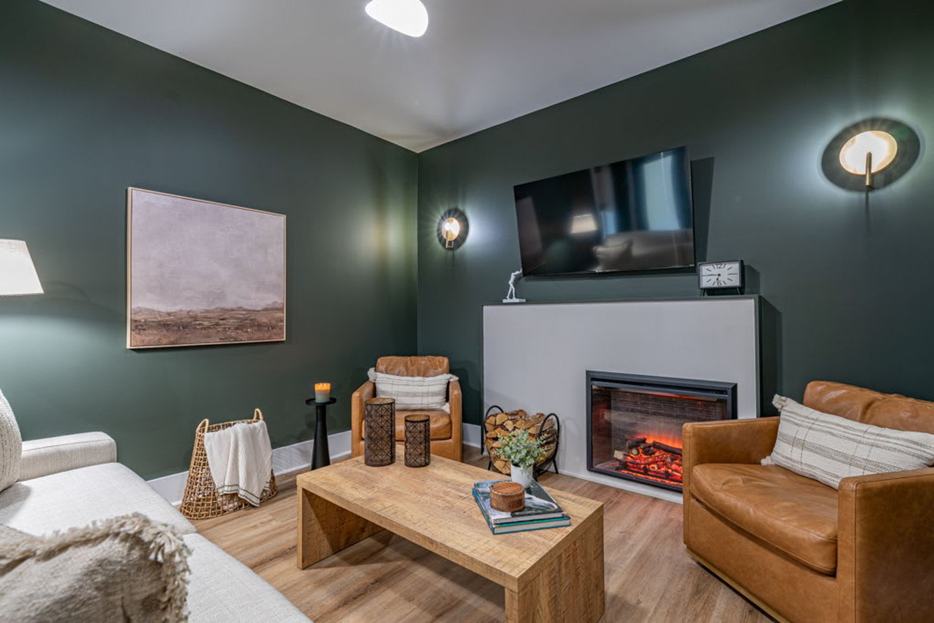 A modern living room with a fireplace, leather sofas, a coffee table, and a flat-screen TV mounted above the fireplace.