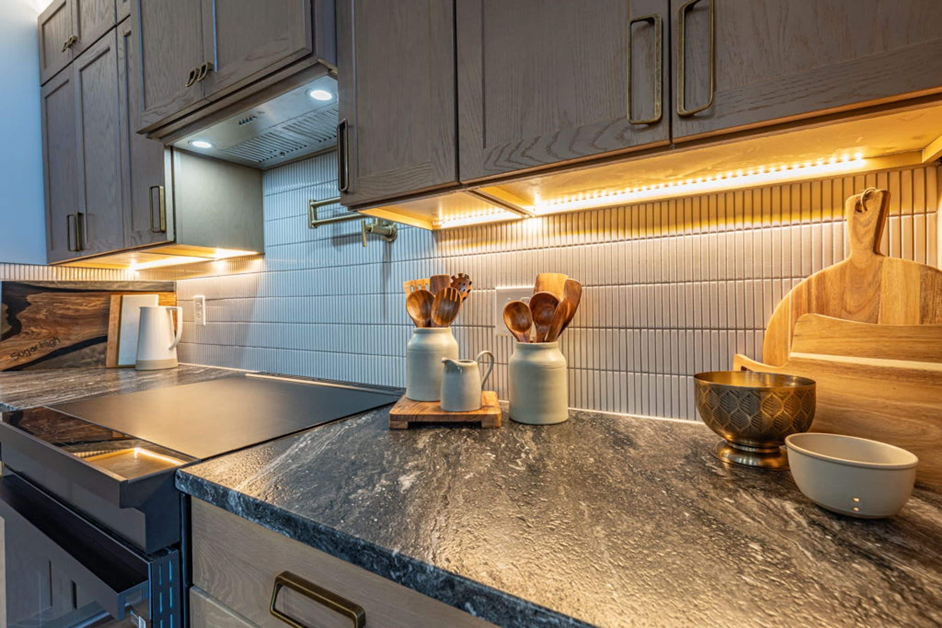 A modern kitchen with a dark countertop, wooden cabinets, and a tiled backsplash.