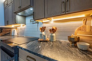Une cuisine moderne avec un plan de travail foncé, des armoires en bois et un pare-feu en carreaux.
