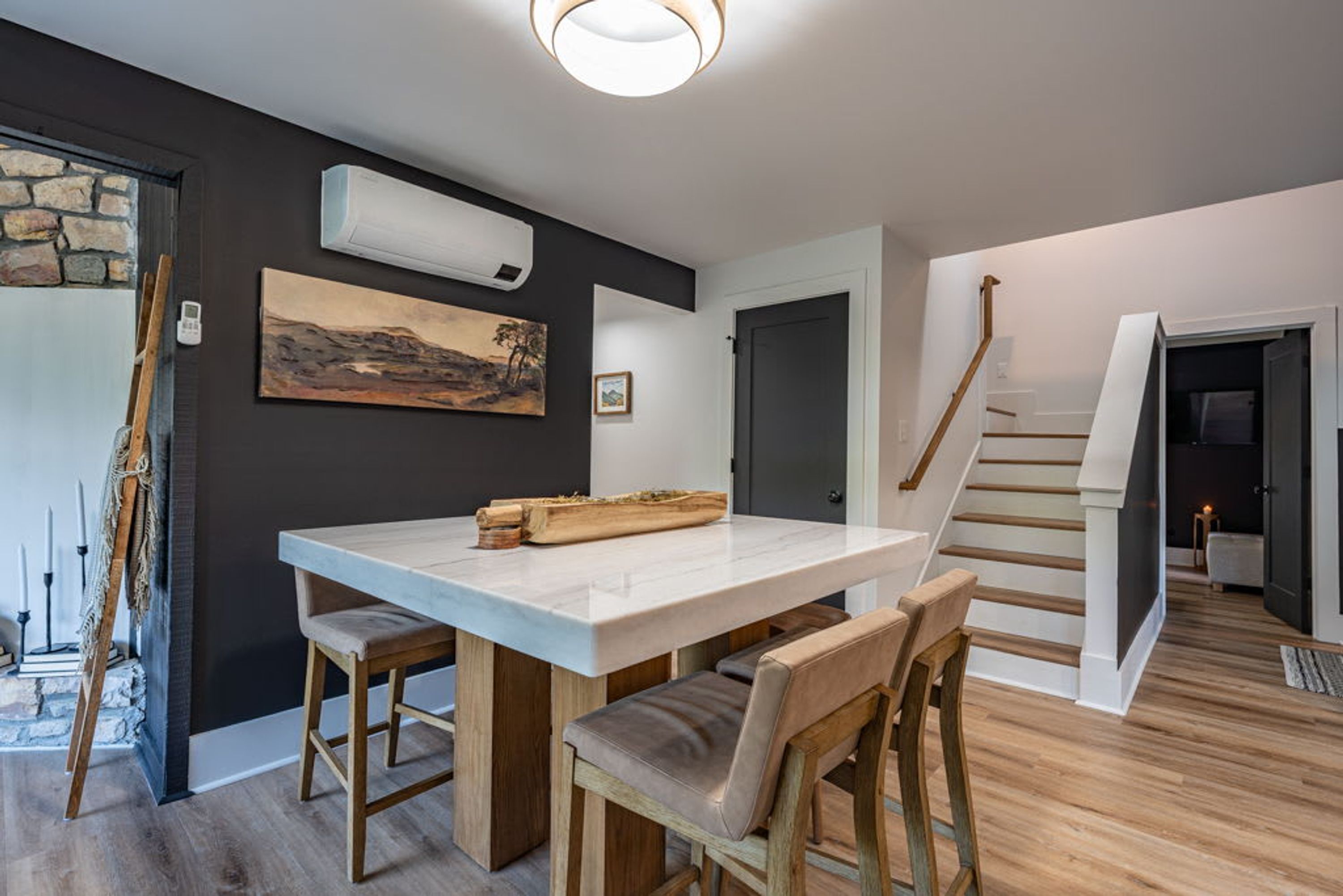 Un intérieur moderne avec une table à manger en marbre, des chaises en bois, un escalier et des œuvres d’art accrochées aux murs.