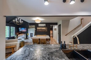 Eine moderne Küche mit Marmorarbeitsplatte, ein Essbereich mit Tisch und Stühlen, ein Wohnzimmer mit Sofa und Fernseher sowie eine Treppe.