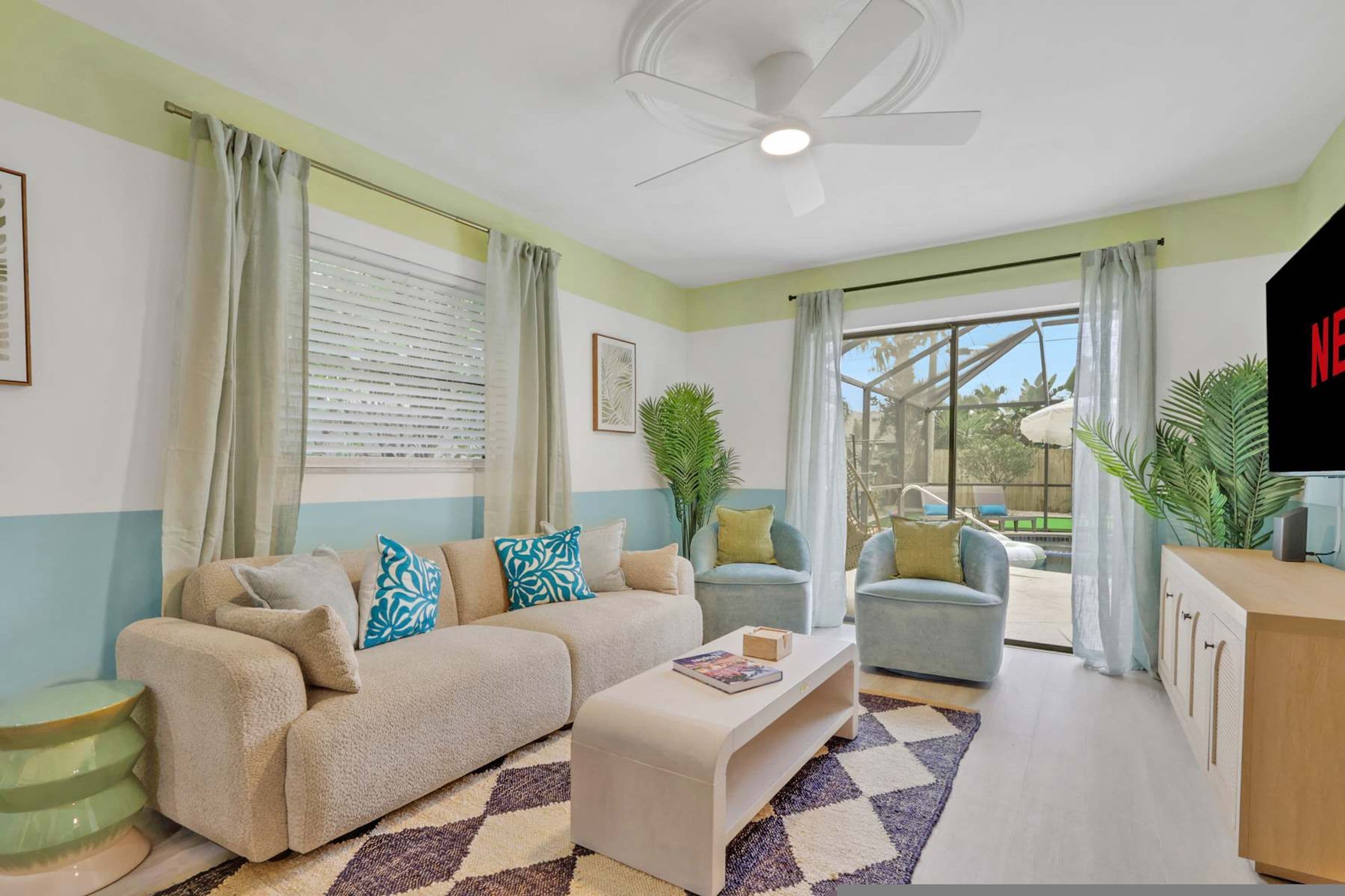 A living room with a sofa, armchairs, a coffee table, a TV, and a view of the outdoors.