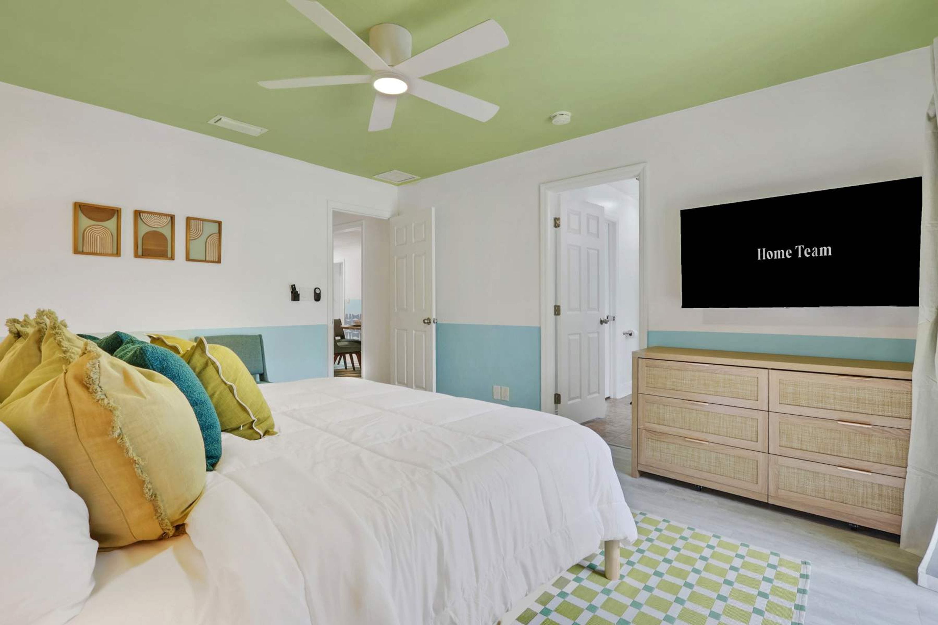 A bedroom with a bed, a ceiling fan, a television, and a dresser.