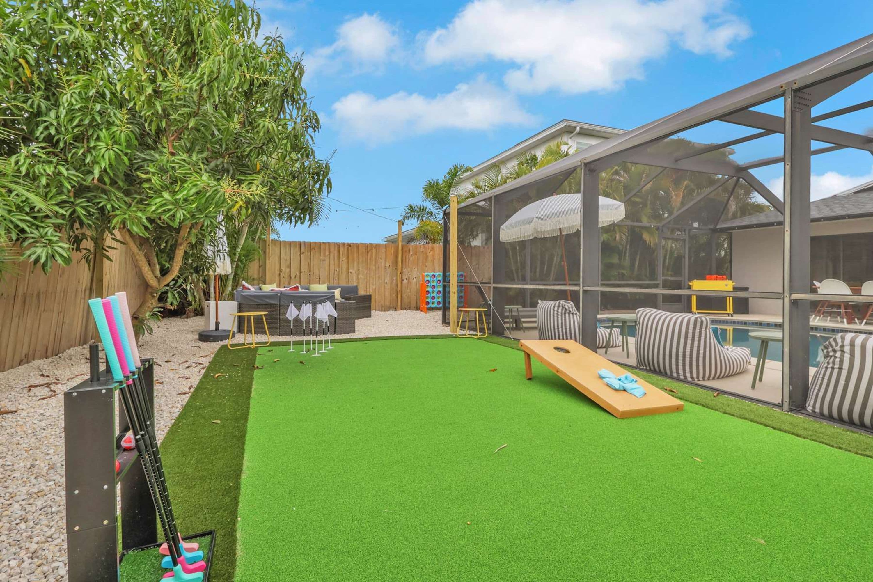 Un patio trasero con césped artificial, piscina y zona de estar cubierta.