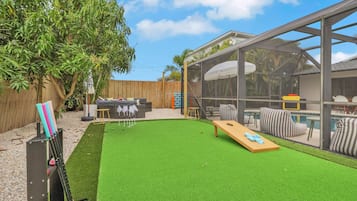 A backyard with artificial grass, a pool, and a covered seating area.