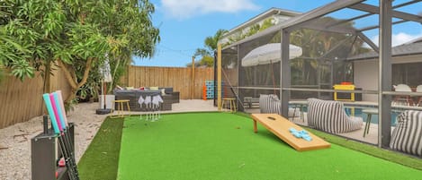 Un patio trasero con césped artificial, piscina y zona de estar cubierta.