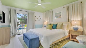 Un dormitorio con cama, mesita de noche, lámpara, ventana con cortinas, ventilador de techo y vista a una zona de piscina exterior.