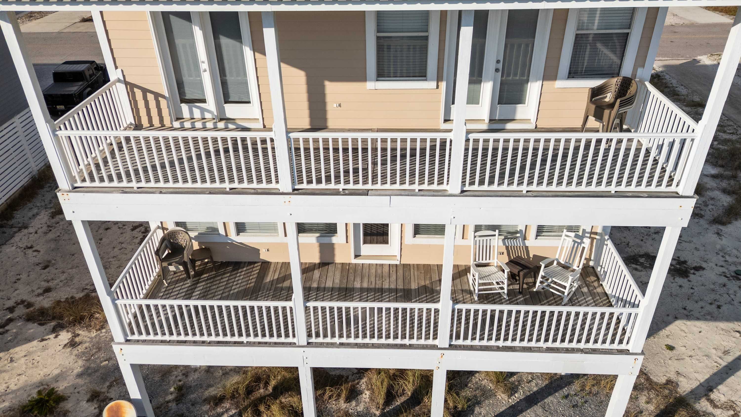 A two-story building with a balcony on each floor, featuring outdoor seating and a vehicle parked nearby.