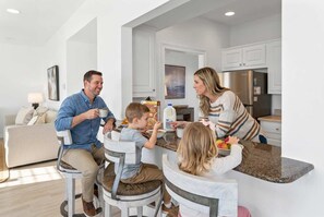 Una familia cenando en una cocina moderna con armarios blancos, una mesa de comedor y una isla integrada.