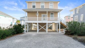 Ein zweigeschossiges Strandhaus mit überdachter Veranda und einer Treppe, die zum oberen Stockwerk führt.