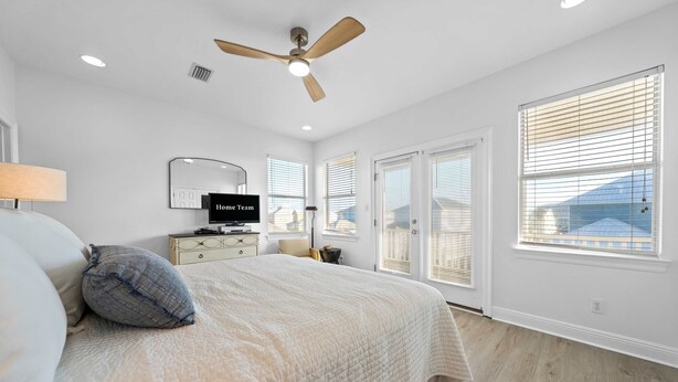 Ein Schlafzimmer mit Bett, Deckenventilator, Fernseher und großen Fenstern mit Jalousien.