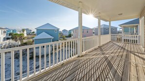 Eine Holzterrasse mit weißer Reling mit Blick auf einen Strand mit Häusern.